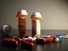 Three orange medicine bottles with white caps and labels with a multitude of differently colored, sized, and shaped pills in front of the bottles.