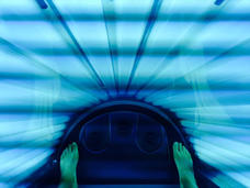 A lit up tanning bed with feet visible at the bottom. The majority of the image is blue and green.