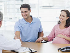 A pregnant person and their partner talking with a doctor at a desk.