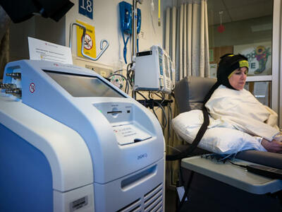 Patient seated in a hospital chair wearing a DigniCap scalp cooling system.