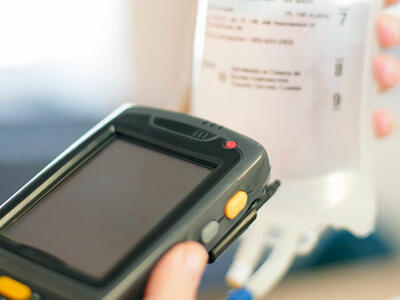 A handheld scanner being used to scan a barcode on an IV bag. 