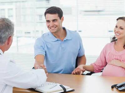 A pregnant person and their partner talking with a doctor at a desk.