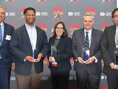Five CURE scholars standing together, each holding an award for lifetime achievement.