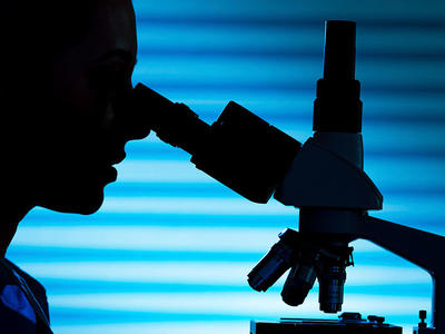 Silhouette of a scientist using a microscope against a background of light blues.