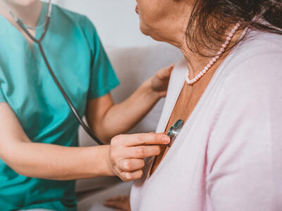 A health provider holding a stethoscope to a woman's chest.
