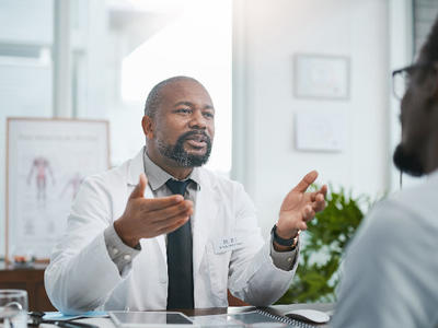 Photo of a doctor sitting at a desk speaking with a patient.