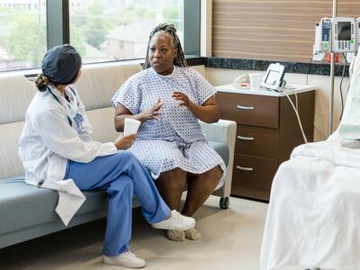 Foto de una mujer de mediana edad en la habitación del hospital conversando con una cirujana.