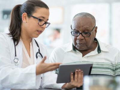 A young female doctor shows information on a tablet computer to an older black male patient.