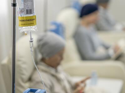A chemotherapy bag hanging and a woman receiving treatment sitting in a chair.