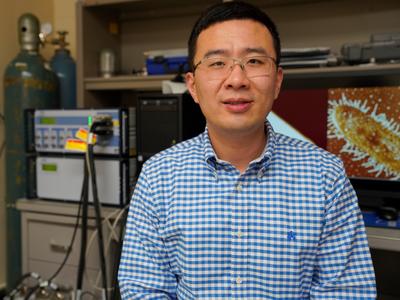 Photo of Dr. Congzhou Wang with a biological image on a computer screen behind him. 