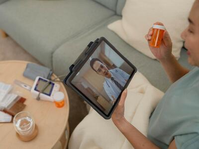 Una mujer sentada en el sofá de su casa sostiene un medicamento en la mano durante una consulta con el médico por videollamada.