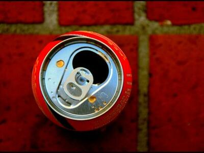 A photo of a red soda can, taken from directly above, sitting on a dark red tiled floor.