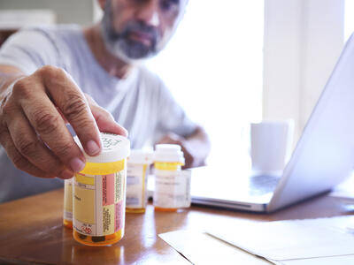 Photo of a man reaching for prescription pill bottles sitting on a table in the foreground.