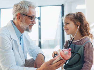 Doctor in white coat with a child patient and stethoscope holding a stuffed animal.