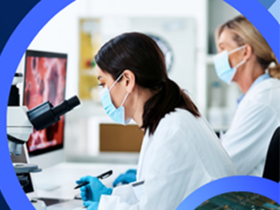 Two women in lab coats and gloves using a microscope.