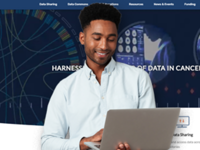 Individual holding a laptop while standing in front of the homepage for datascience.cancer.gov website.