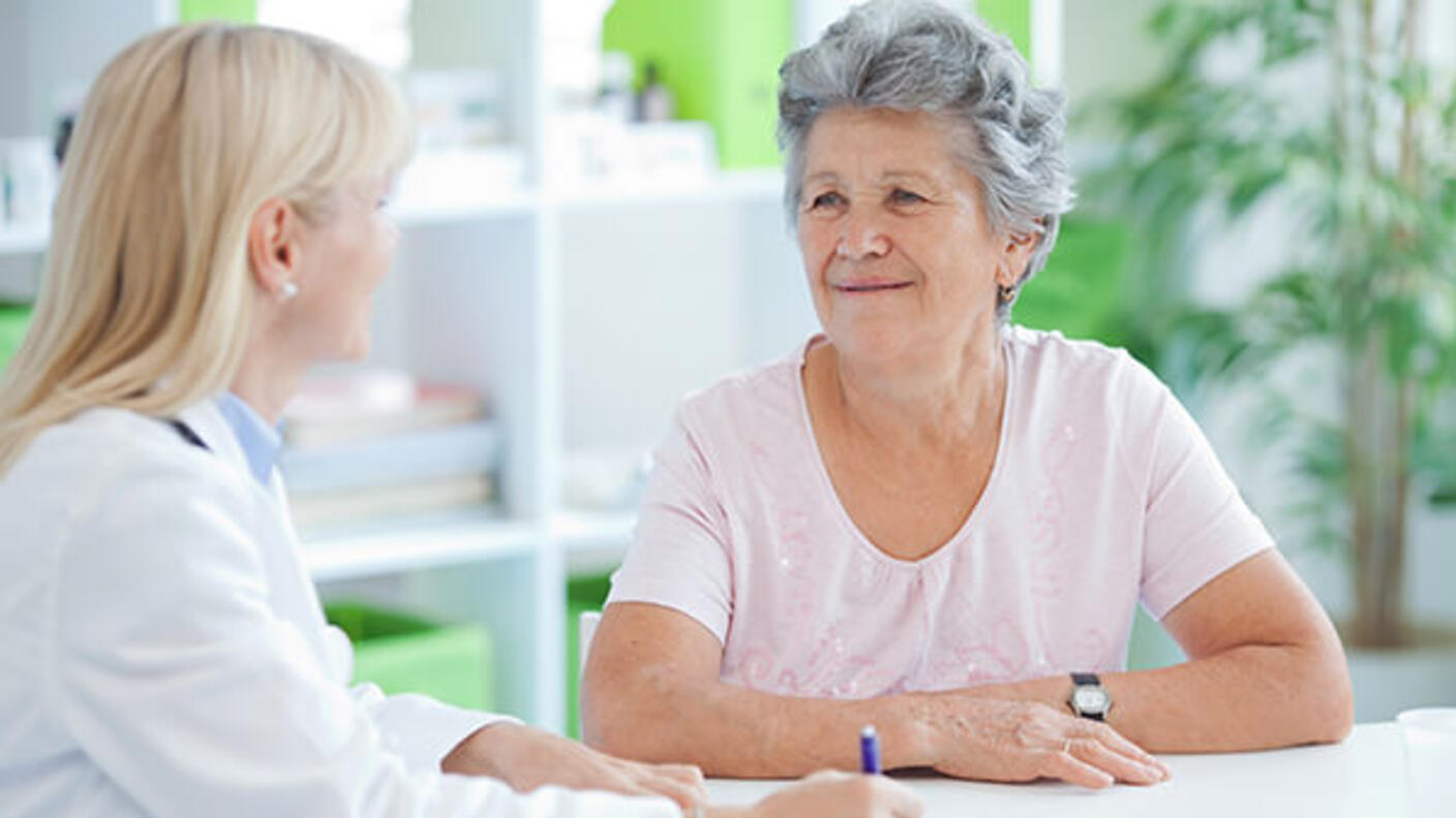 Medical professional writing notes and talking to a patient.