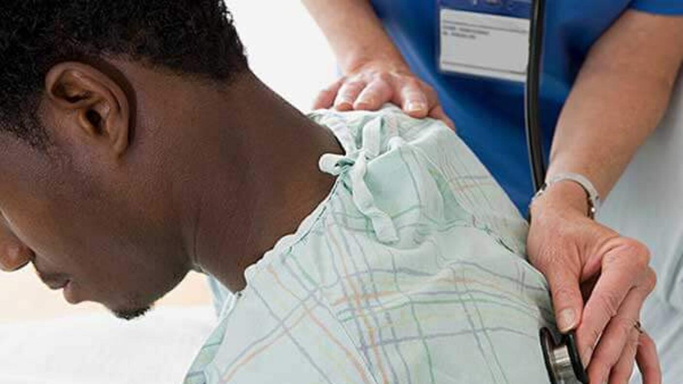 Healthcare provider's hands placing a medical device on a patient's back over their clothing as part of a medical examination or treatment.