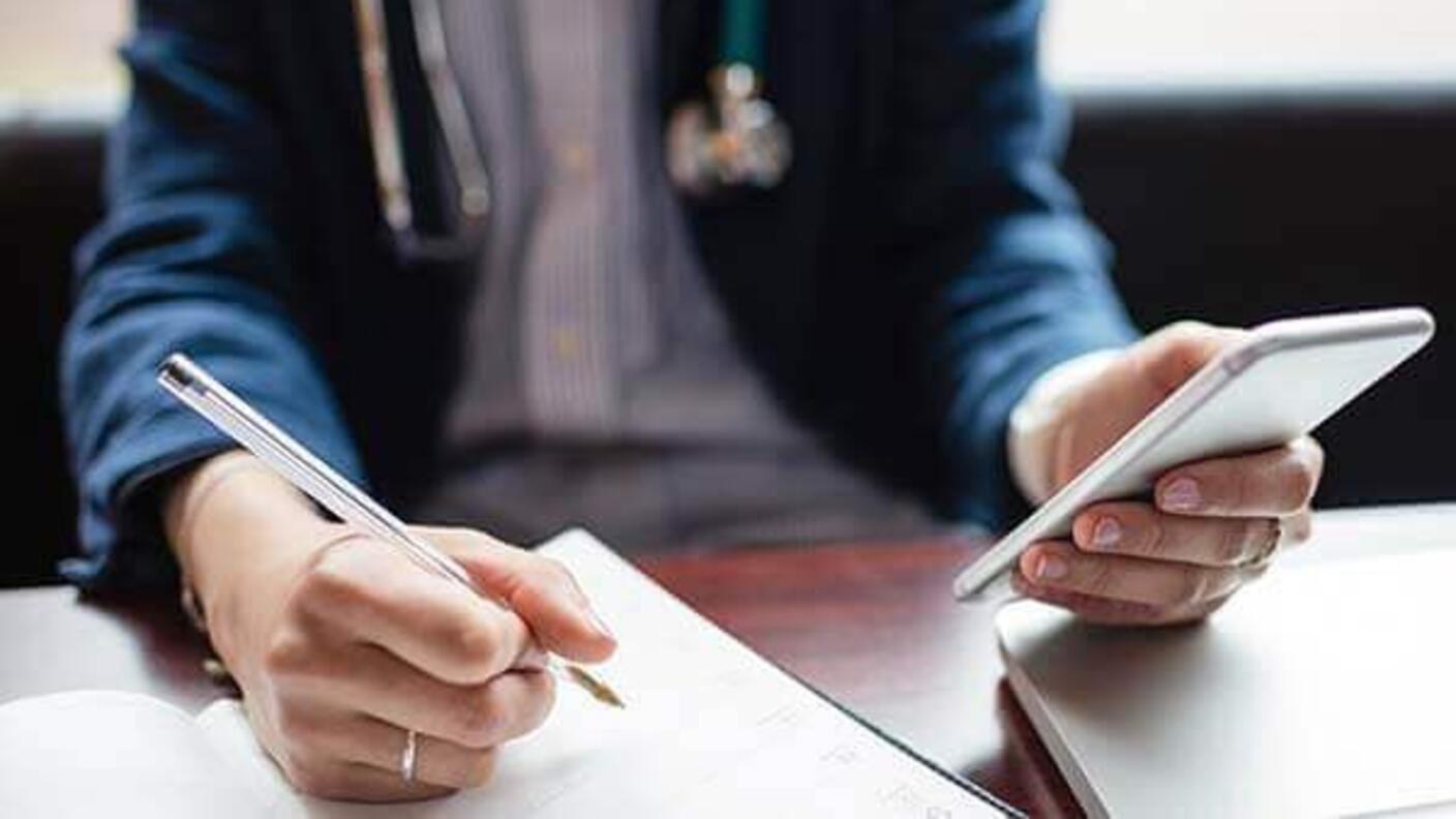 A medical professional writing and using a mobile phone.