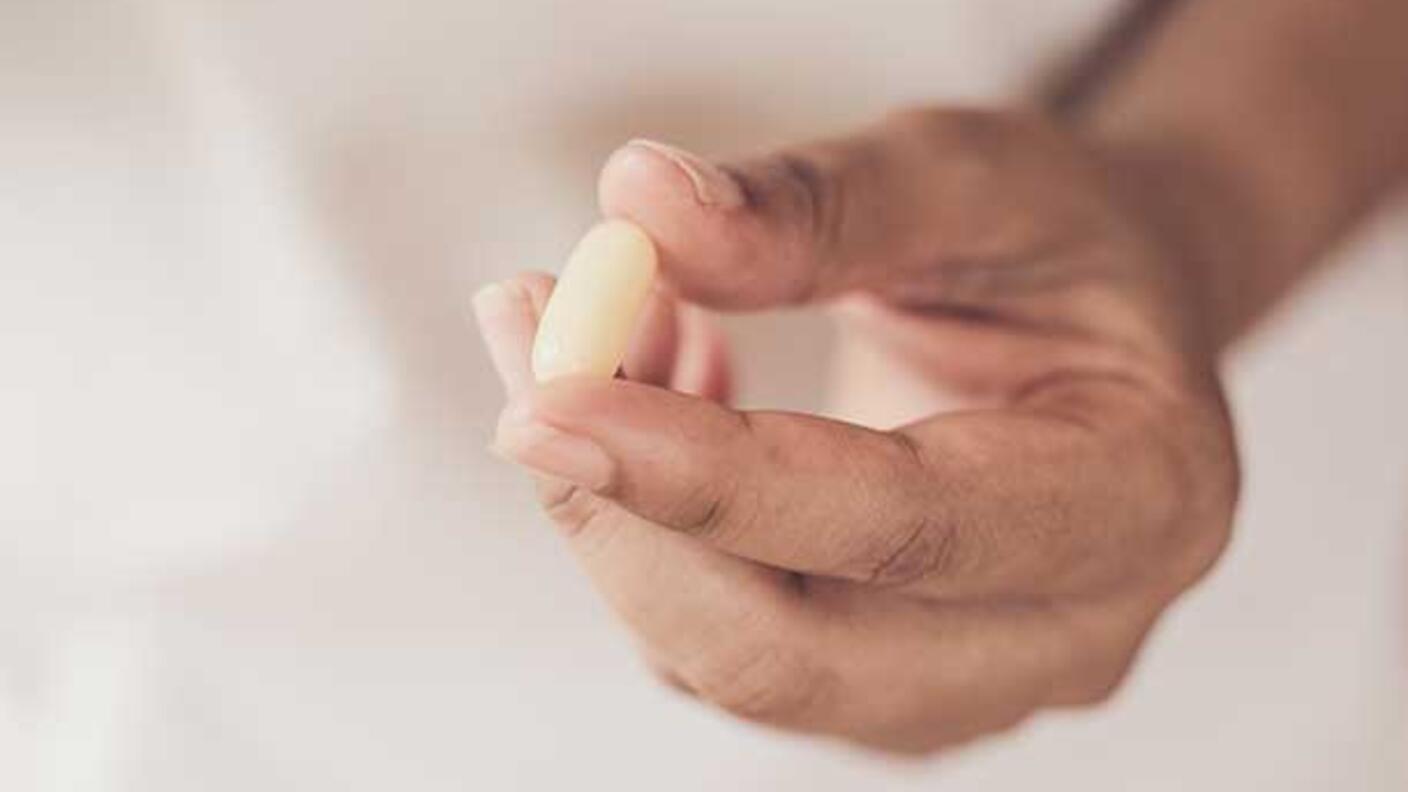 Close-up of hands holding a yellow pill against a white background.