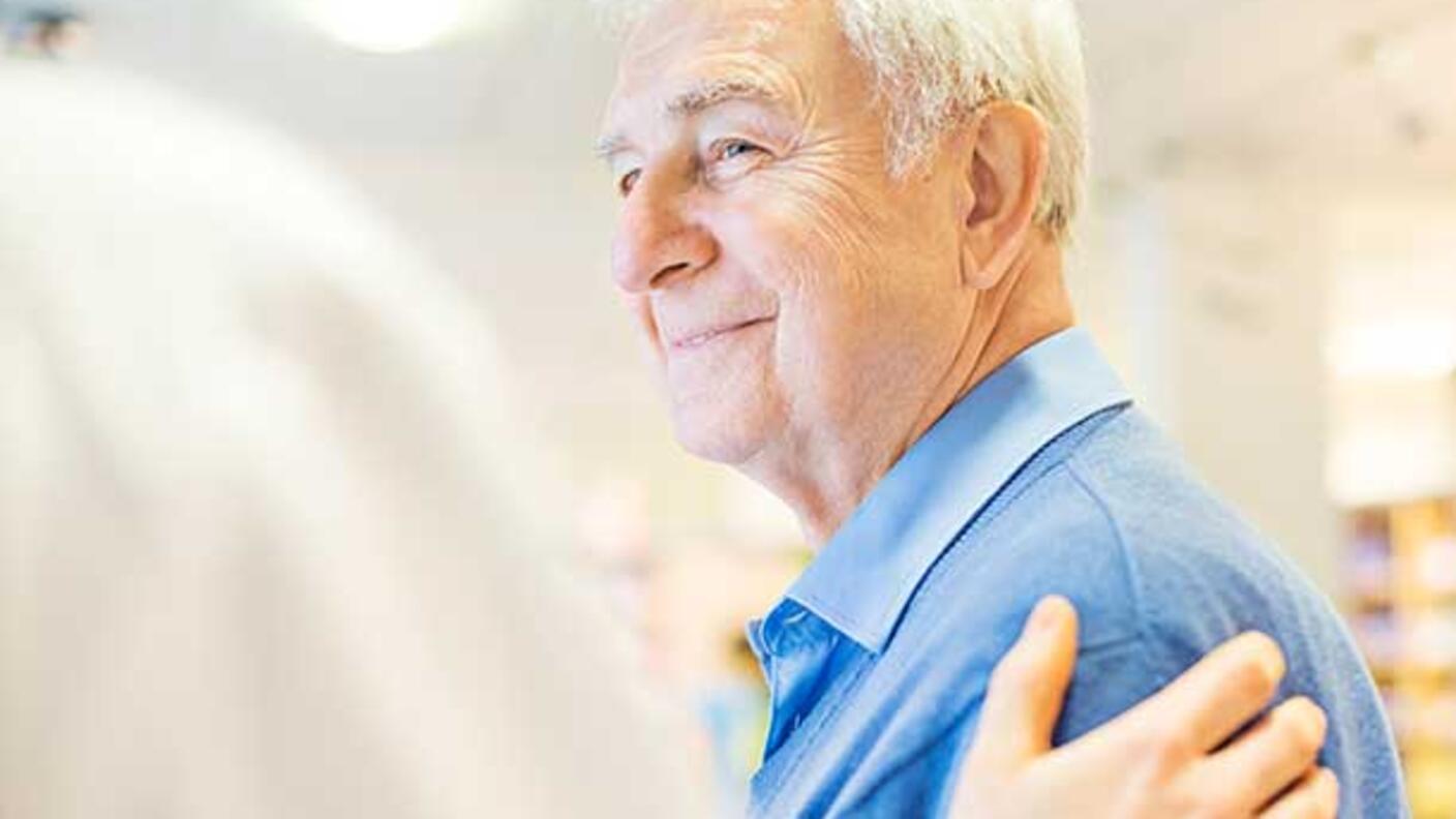 A doctor puts his hand on an older man's shoulder.