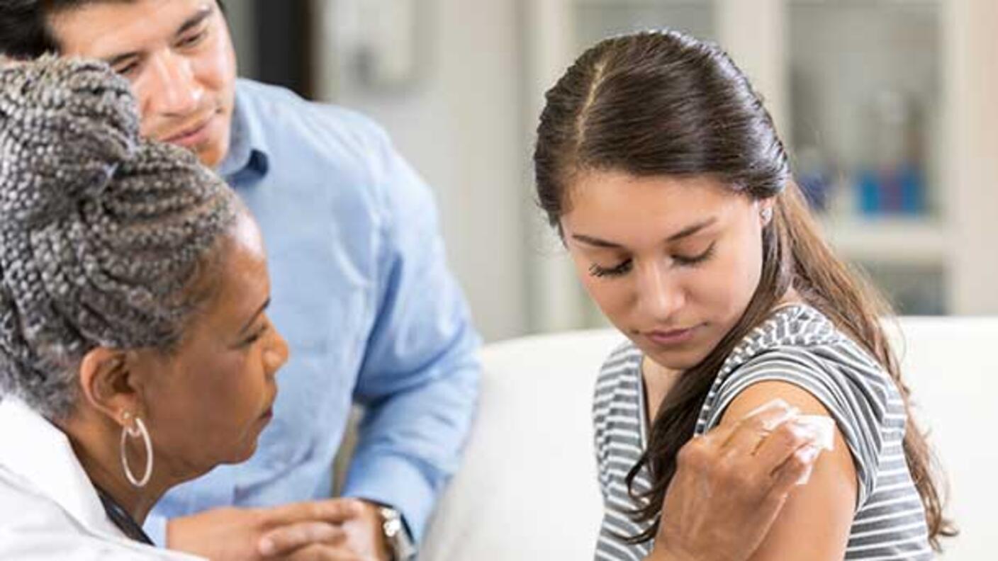 A teenage girl receiving a vaccine in her upper arm from a nurse.
