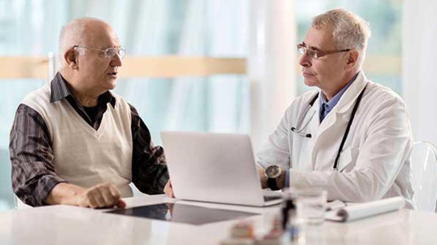 Male patient and male doctor meet with laptop open between them.