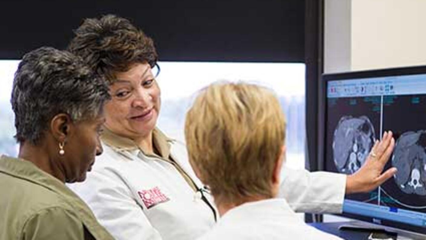 Photo of three women reviewing medical scans in an office. 