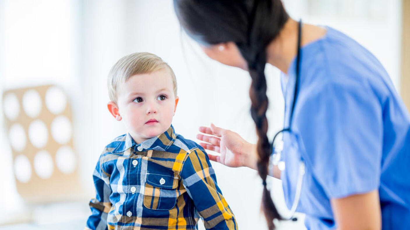 Female health care provider talks to young boy seated next to her.