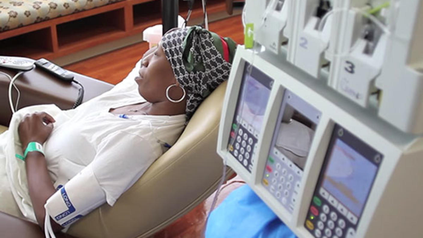 Woman wearing headscarf and reclining in chair receives cancer treatment at medical facility.