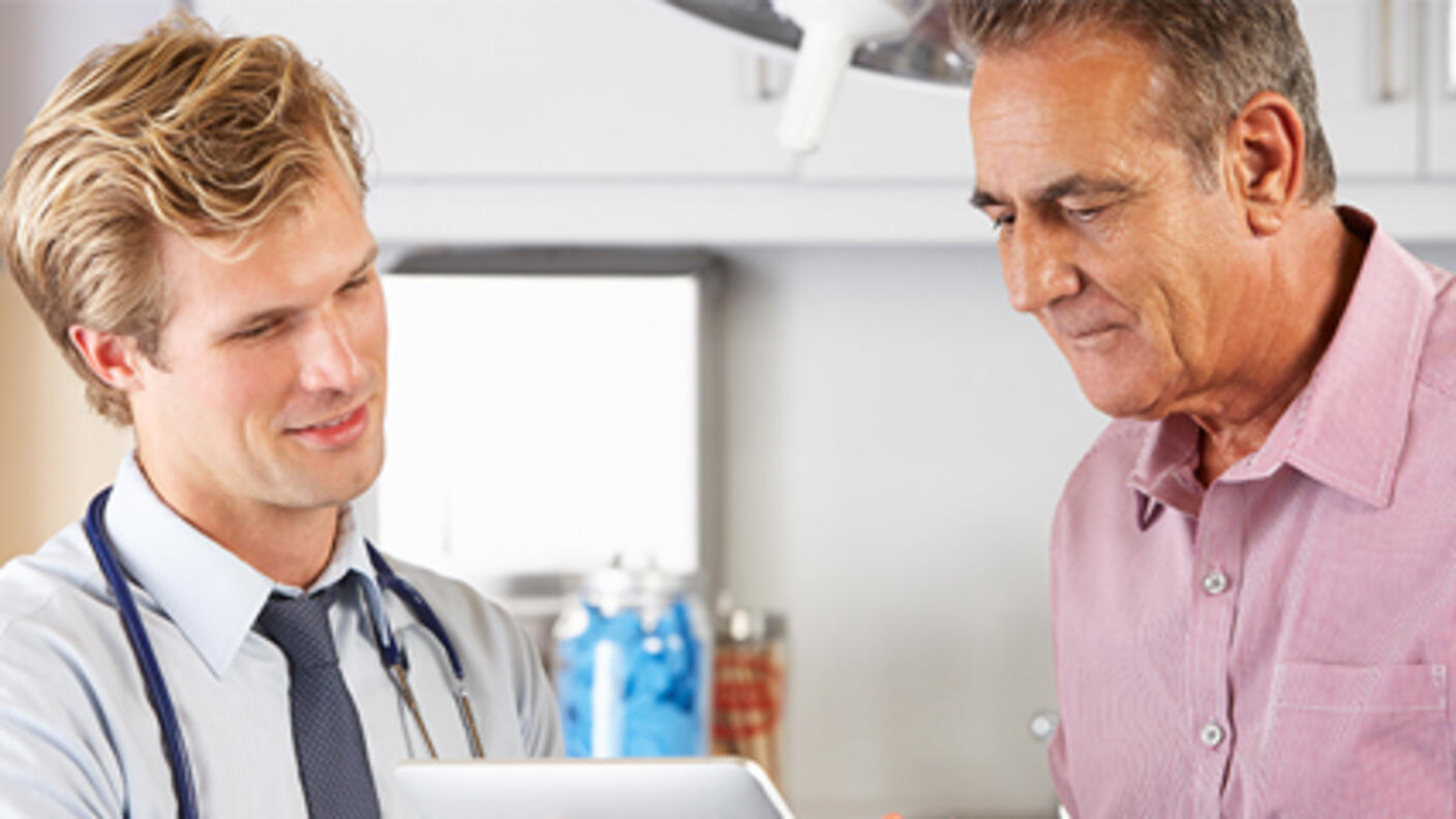 Male doctor shows male patient information on a tablet computer.