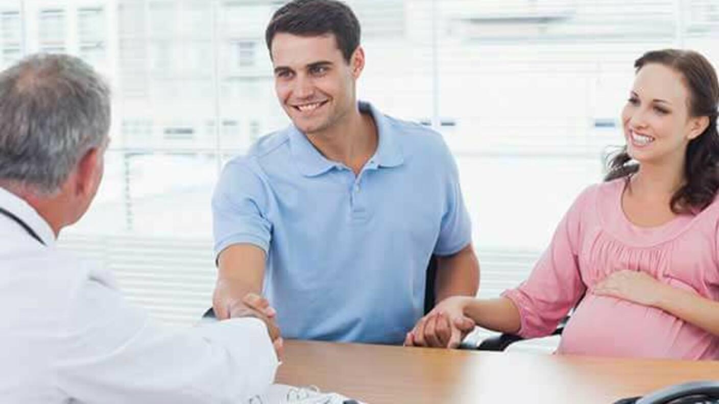 A pregnant person and their partner talking with a doctor at a desk.
