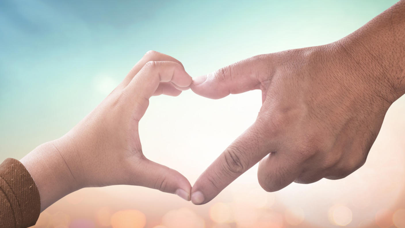 Close-up of child and adult hands joining fingertips to form heart shape