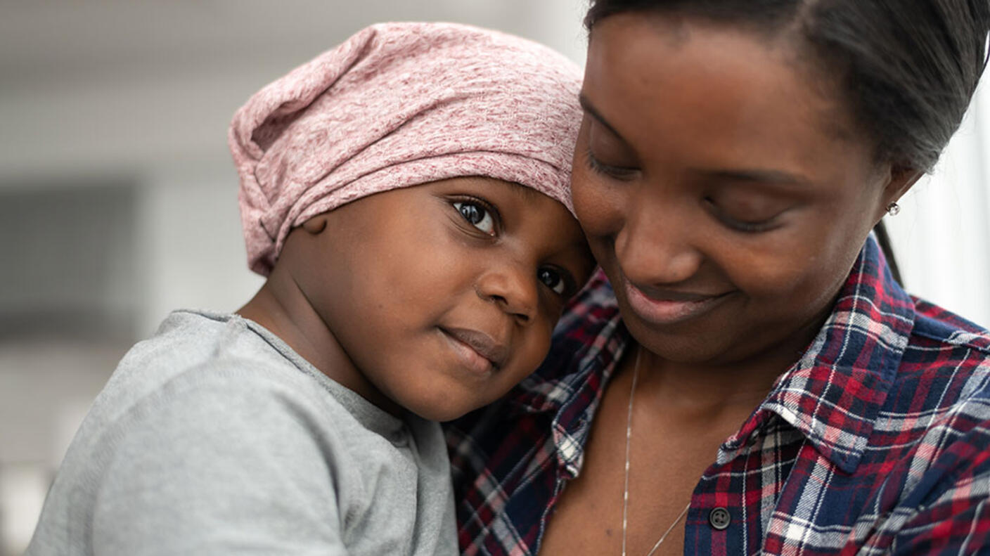 Child wearing head scarf cuddles and rests head on shoulder of a woman