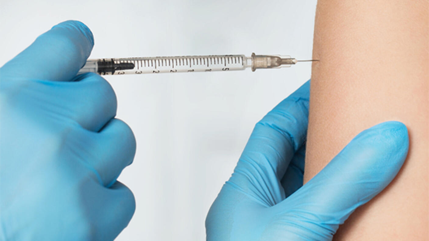 Photo of gloved hands administering an injection into a patient's upper arm.