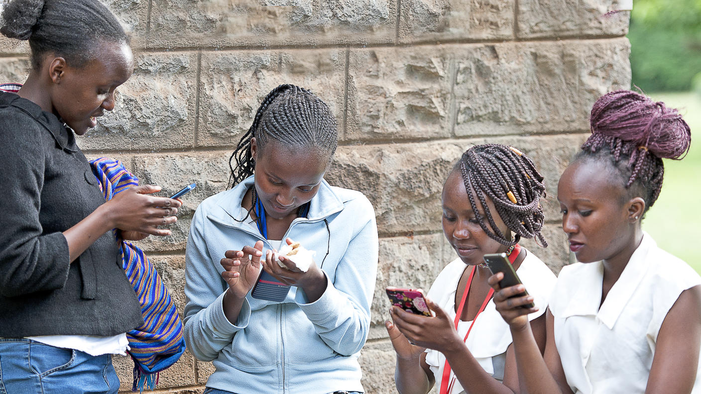 Several Kenyan girls looking at their cell phones.