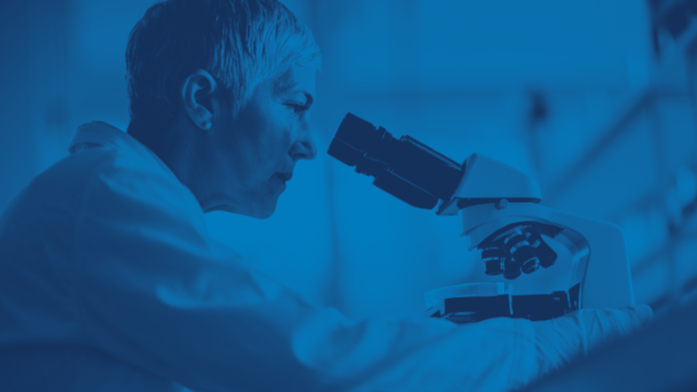 A scientist wearing a lab coat examines a sample under a microscope in a laboratory setting. The image has a blue overlay.