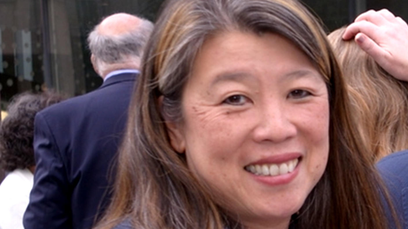 An Asian woman with light skin tone wearing a blue blazer (Dr. Mignon Lee-Cheun Loh) smiles at the camera at an outdoor conference event. 