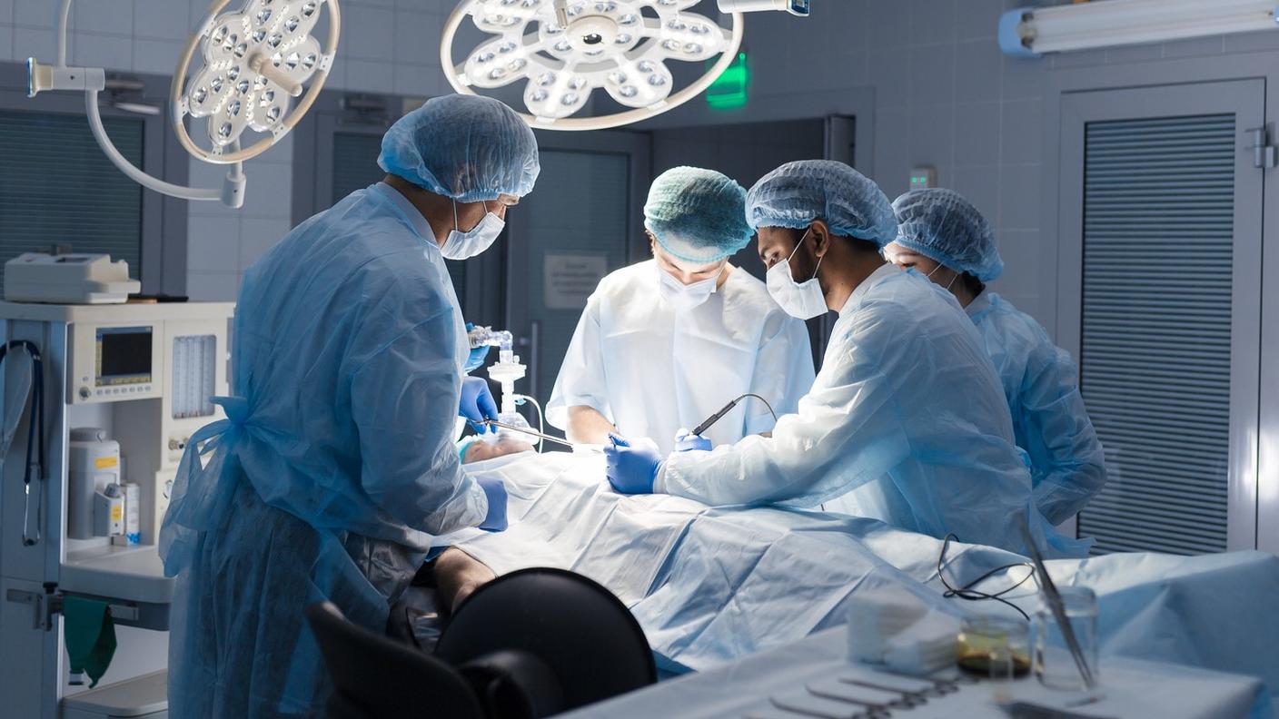 A surgical team of 2 men and 2 women standing over a patient on a table in a surgery suite.