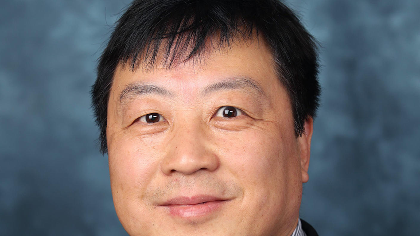 A man (Dr. Xiao-Nan Li) with dark hair and brown eyes wears a striped collared shirt, tie, and dark jacket and smiles at the camera.