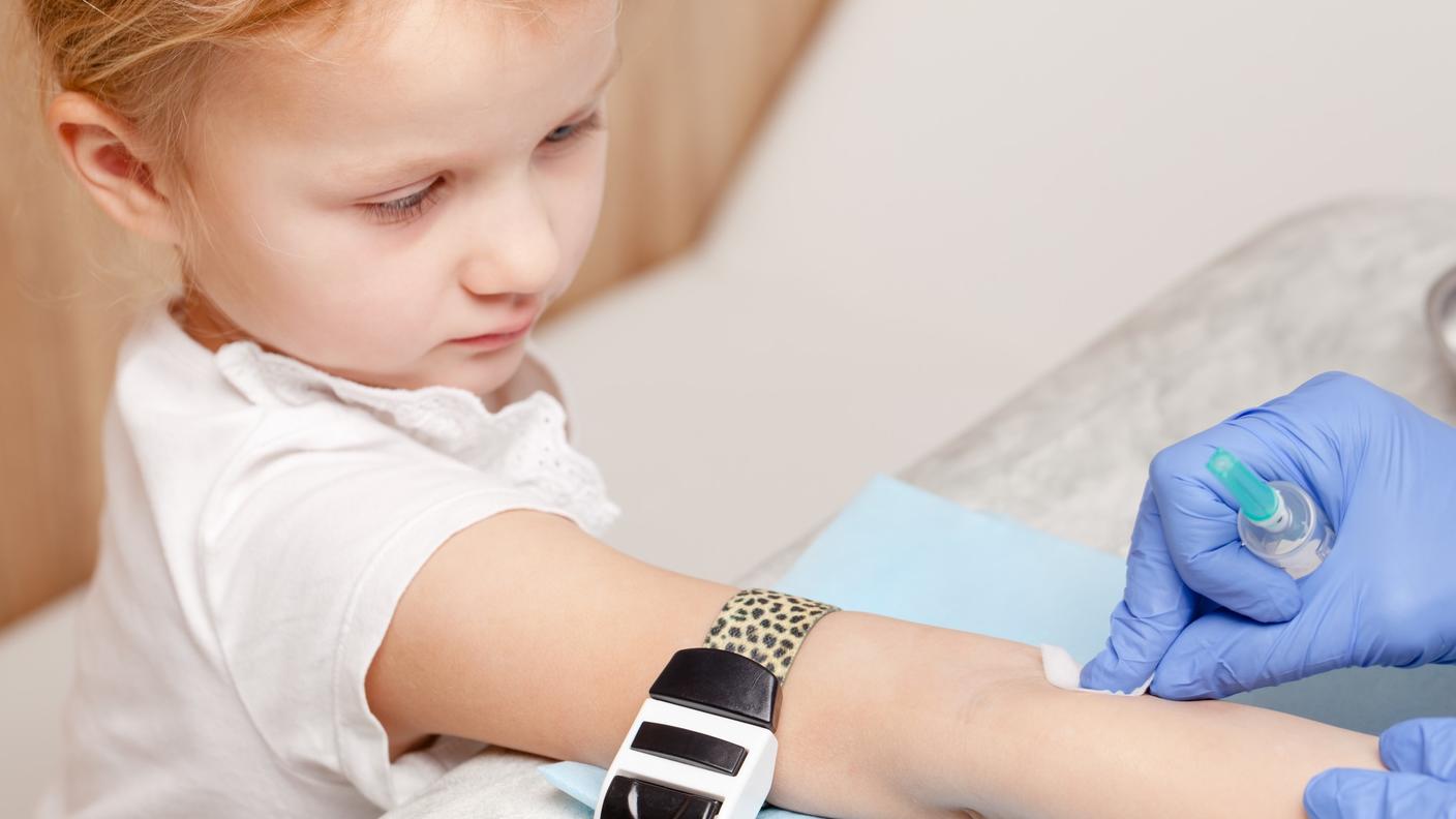 A young girl with her arm out and gloved hands cleaning a spot on her arm with a swab.