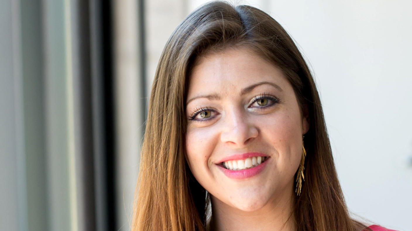 A woman, Dr. Aubrey Hubbard, with long brown hair and hazel eyes wearing a pink blouse and long earrings stands smiling at the camera.