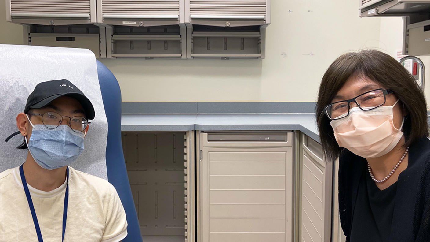 A doctor, Dr. Alice Chen, with short, dark hair wearing glasses and a surgical mask sits next to a patient wearing a hat, glasses, surgical mask, and yellow t-shirt in an exam room.