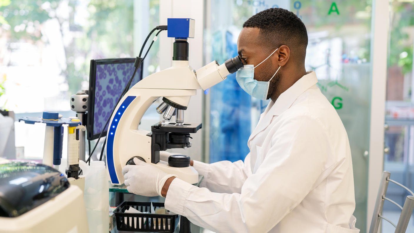 Man in a white lab coat looking into a microscope