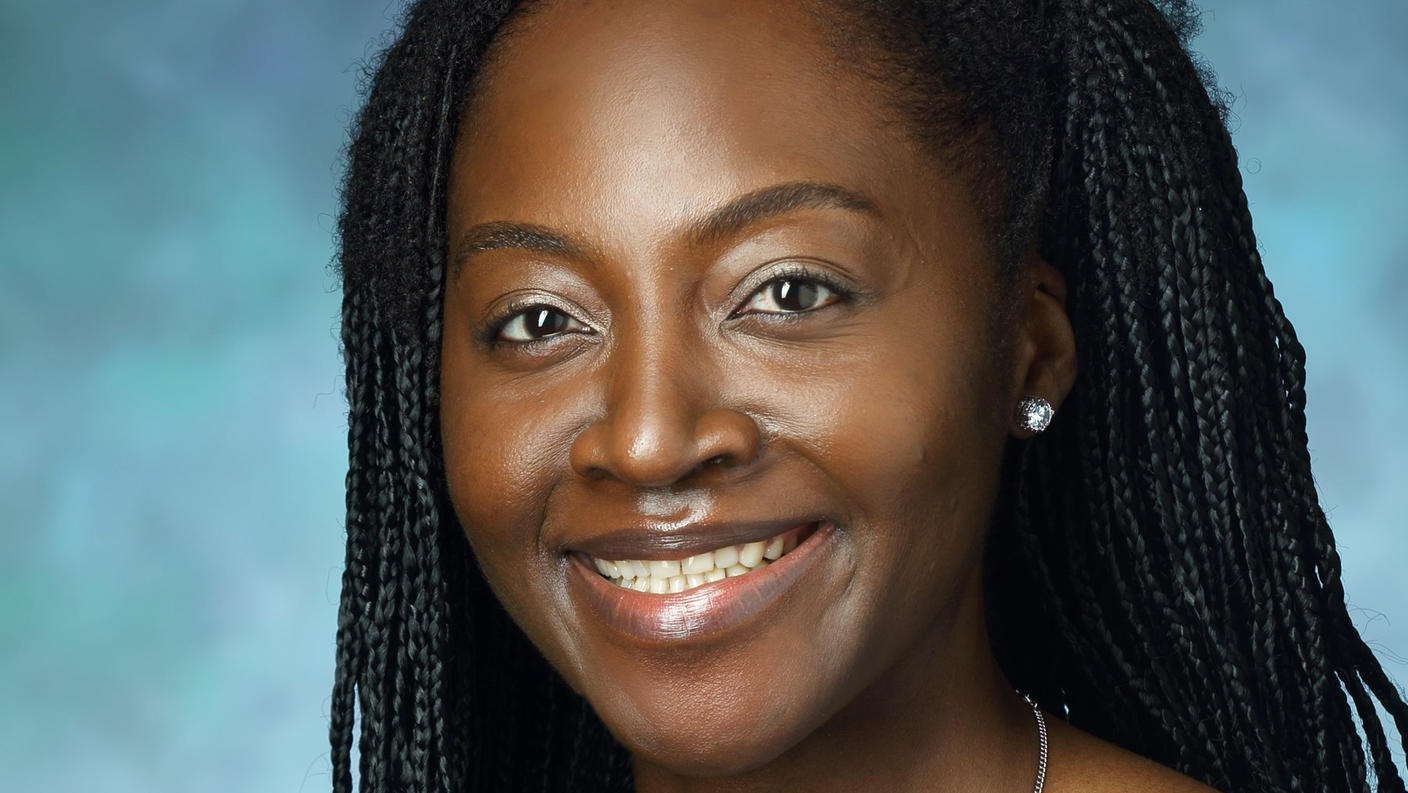 A woman, Dr. Ethel Ngen, with braided black hair and dark brown eyes wearing a light blue blouse smiles at the camera.
