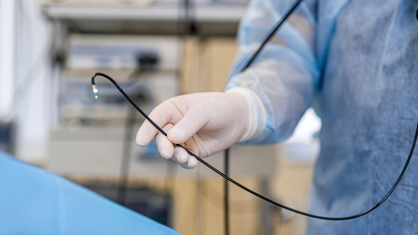 A partial image of a doctor holding a colonoscope near a patient in the endoscopy suite.