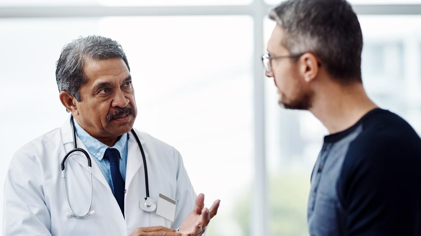 An older male doctor talking with a middle-aged male patient.