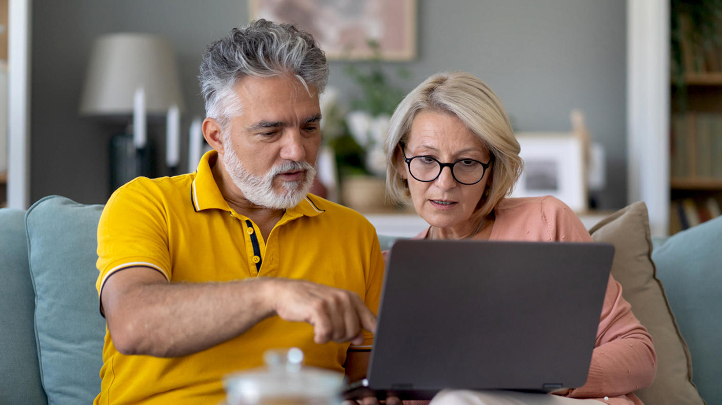 A man and woman researching information on a laptop at home. 