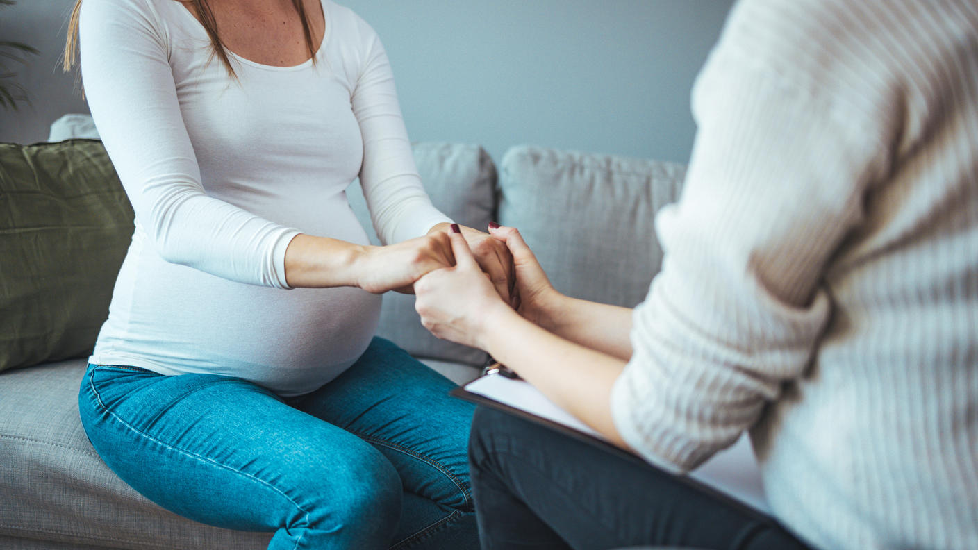A woman with a clipboard holding the hands of a pregnant woman.