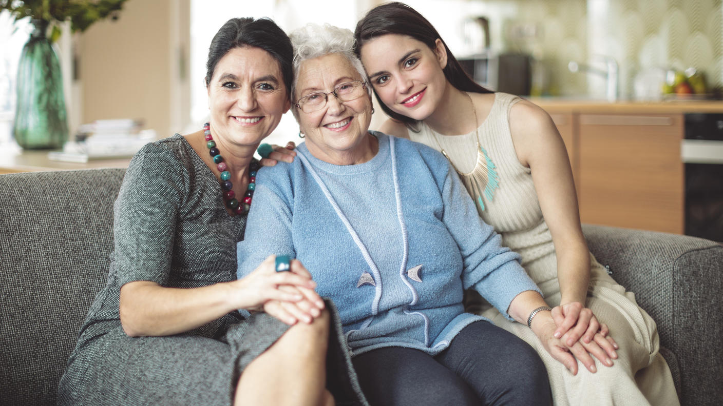 A senior woman sitting in between an older woman and a younger woman on a sofa.